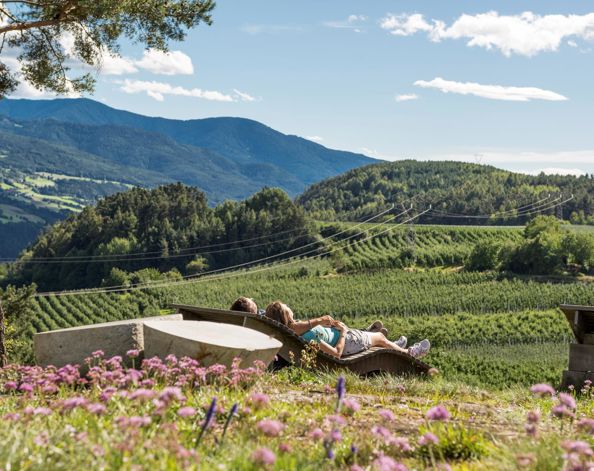 Two people are relaxing on a wooden sun lounger