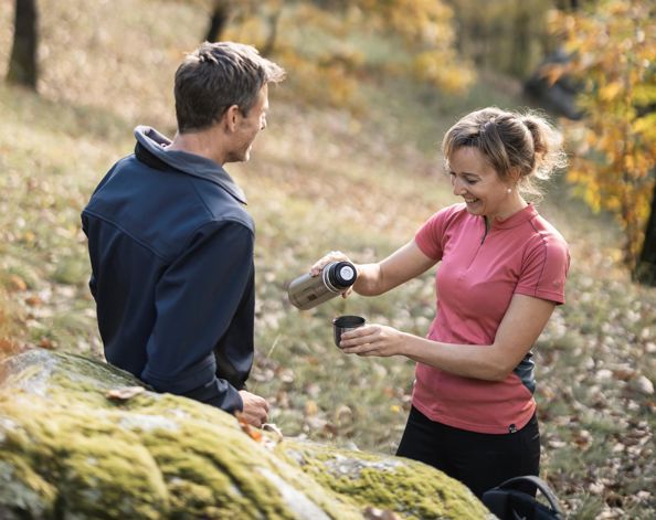 Ein Mann und eine Frau pausieren im Wald mit einer Tasse Tee