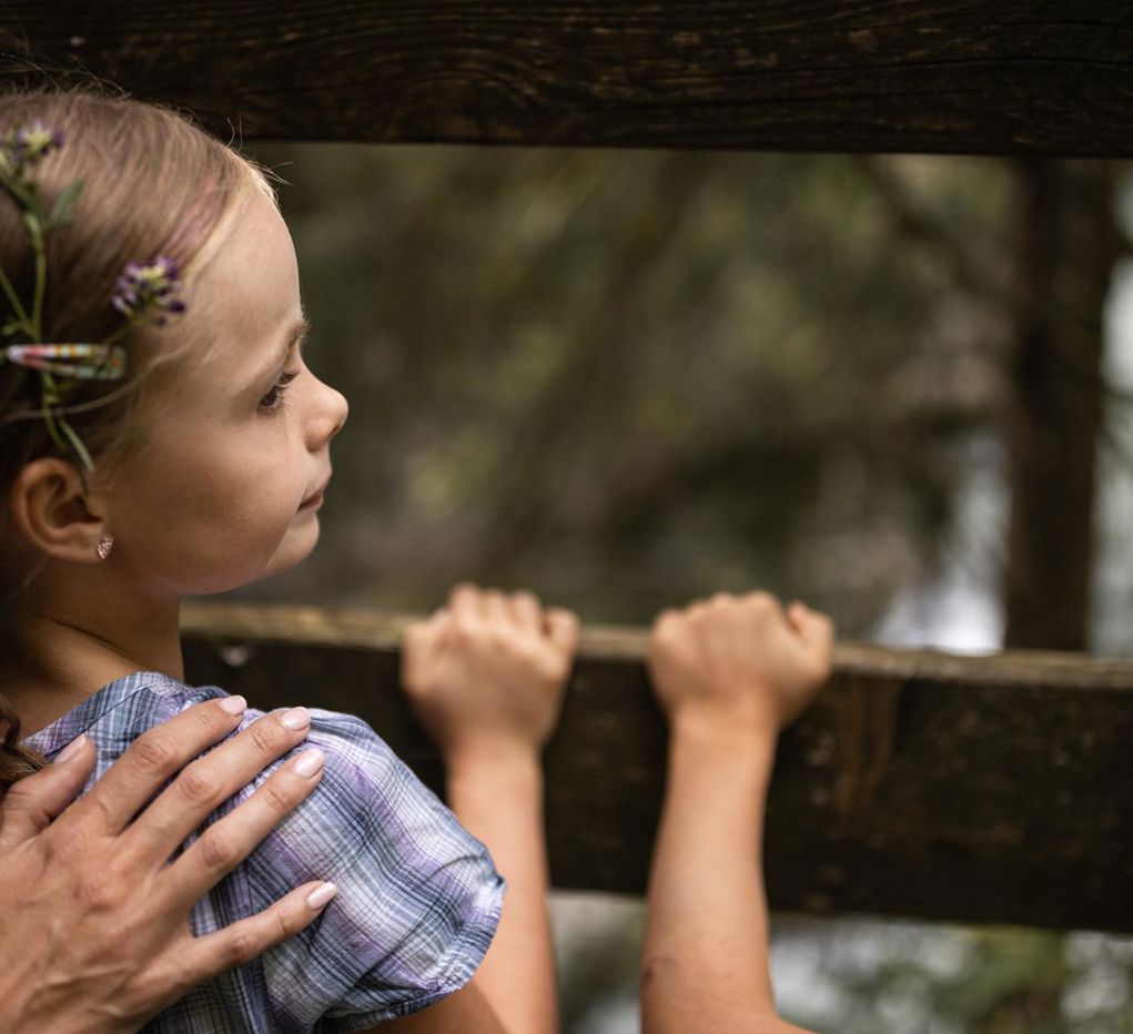 A child is standing by a fence