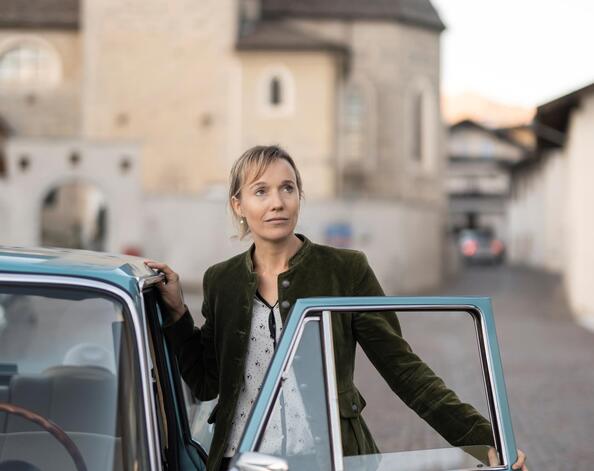 A woman is standing next to the door of a classic car