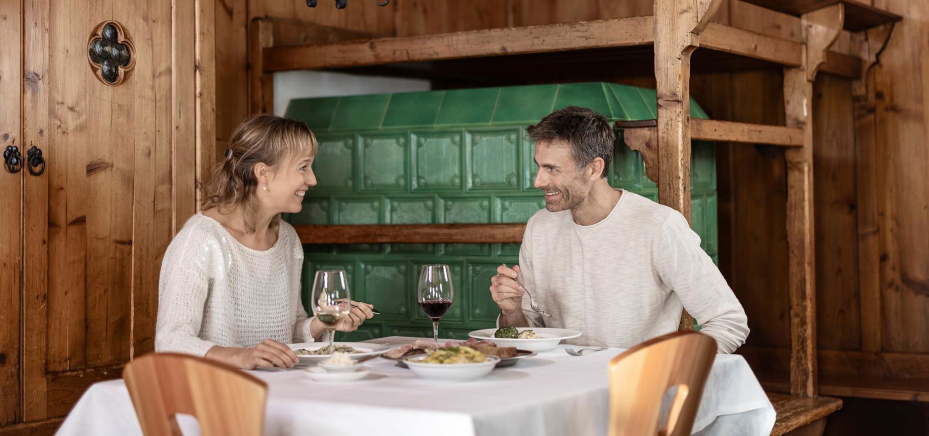 Un uomo e una donna siedono in una stube accogliente e gustano insieme schlutzkrapfen e canederli